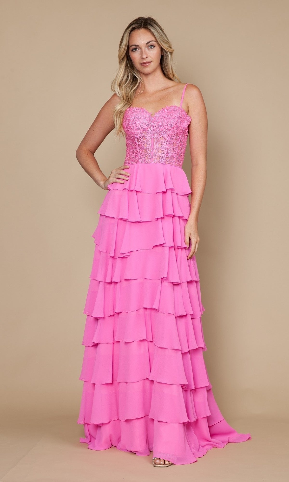 A woman poses against a beige background wearing the Long Tiered Corset Prom Dress: Poly USA 9698—a bright pink A-line gown with thin straps and a fitted, beaded corset-style bodice.